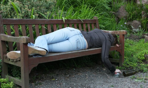 Ung berusad person sover på en parkbänk med en spritflaska bredvid