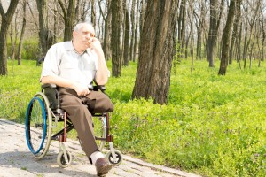 Pensive elderly amputee sitting alone on a rural pathway in his wheelchair with his chin resting on his hand staring into the distance