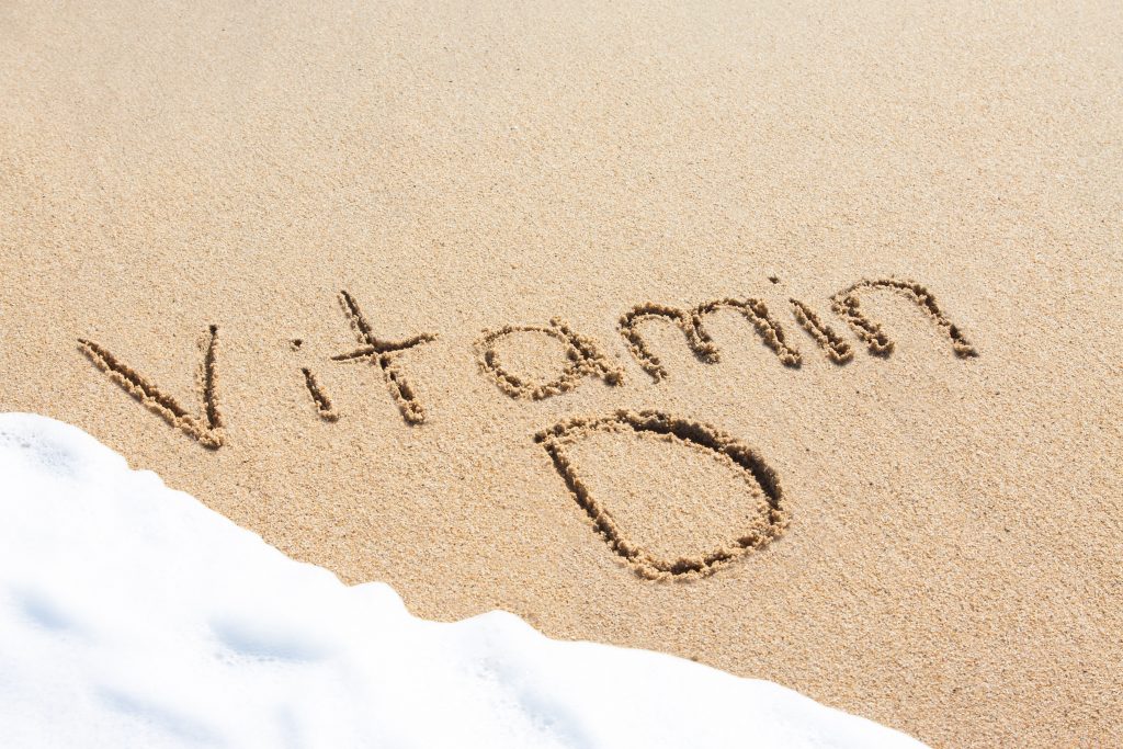 Vitamin D written in the sand with foam from a wave washing up