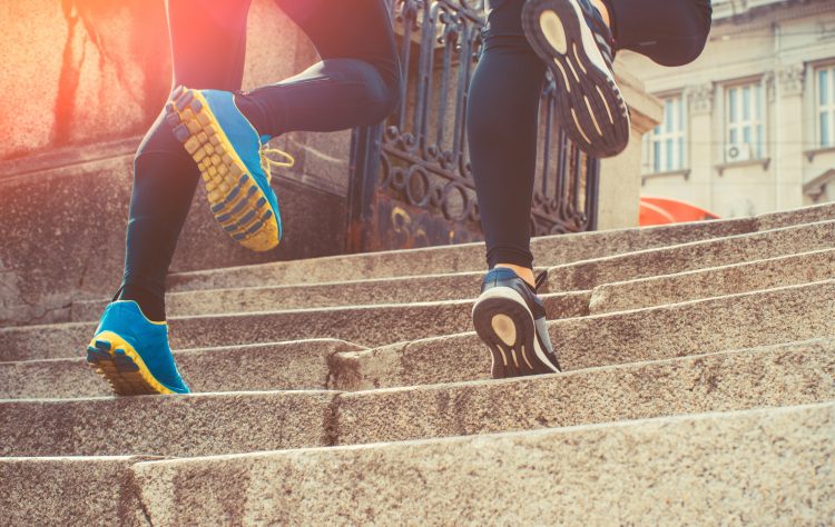 Couple wearing sportswear and jogging on steps in city.