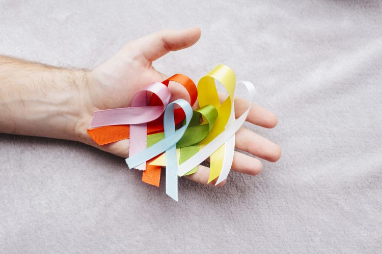 Bild på hand som håller band i olika färger som alla representerar olika cancertyper.