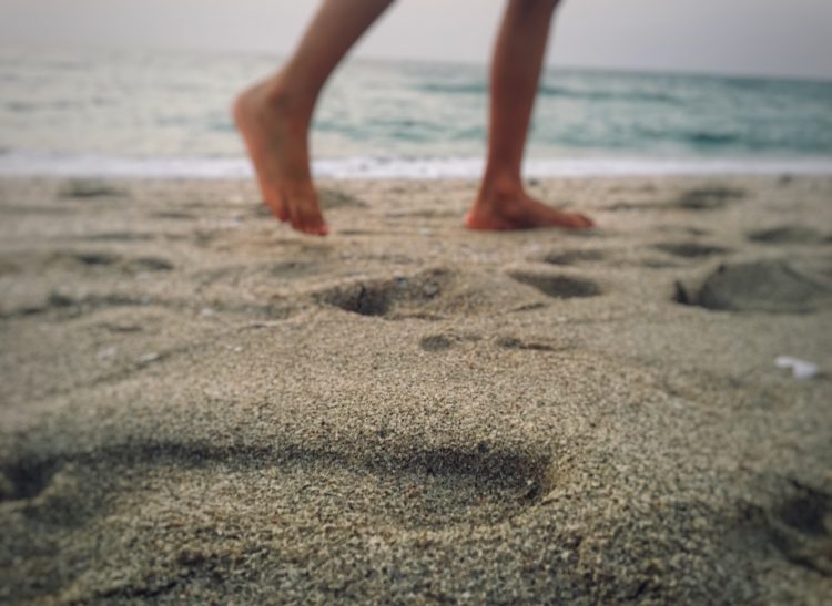 fötter på en person som går på en sandstrand och lämnar spår efter sig