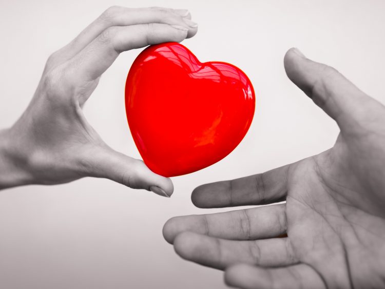 bilden visar två händer, en som håller i ett rött stiliserat hjärta och är på väg att lämna över till den andra handen.