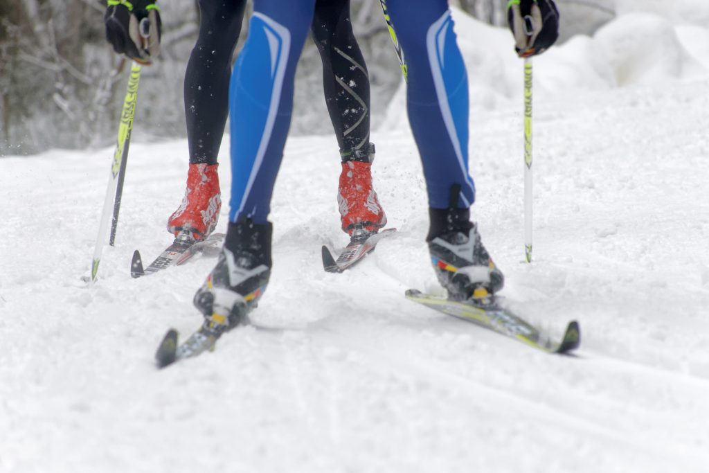 Stavar och två par ben av skidåkare i snö.