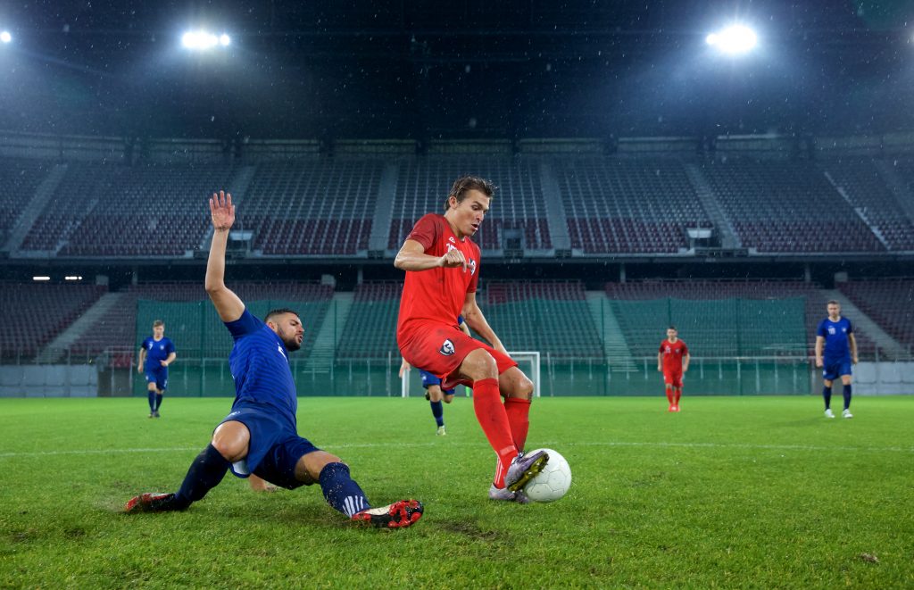 På bilden ses två fotbollsspelare som kämpar om bollen. I bakgrunden syns tomma läktare