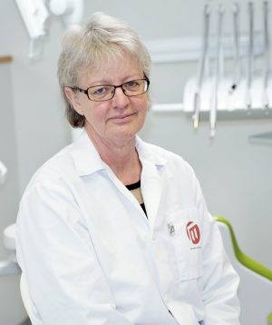 porträttbild på Eva Wolf iklädd vit labbrock. I bakgrundens ser man olika tandläkarinstrument