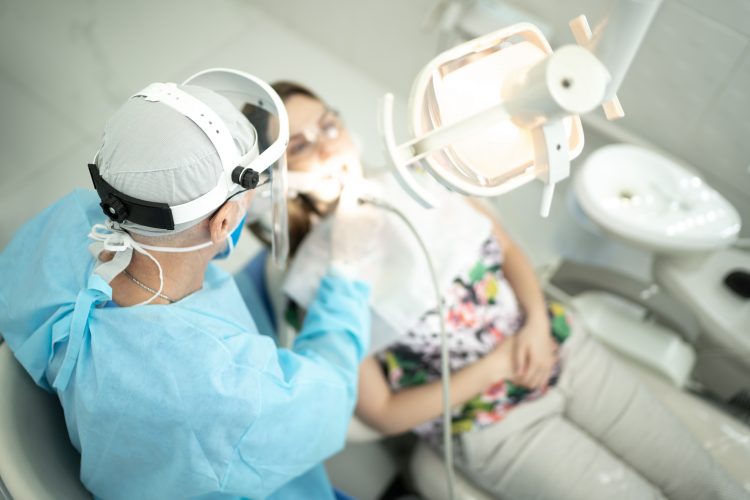 En tandläkare undersöker tänderna hos en ung kvinna som sitter i en tandläkarstol.