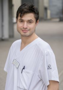 porträttfoto av Josef Dankiewicz i halvfigur. Han är klädd i vit kortärmad sjukhusskjorta med en namnbricka på. Han har mörkbrunt kortklippt hår
