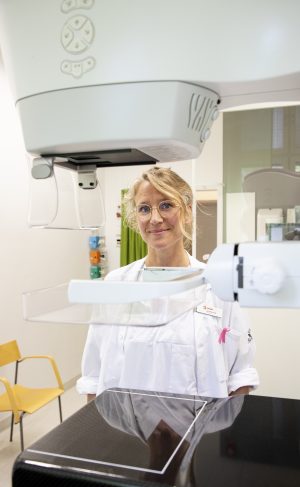 Kvinna i vitsjukhusrock framför mammografi-apparat.