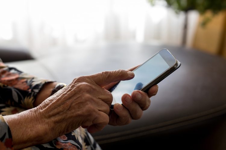En gammal persons händer håller i mobil.