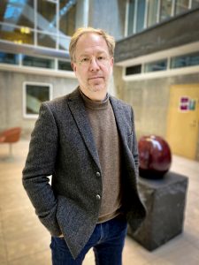 Man i tjockare kavaj och brun tröja.