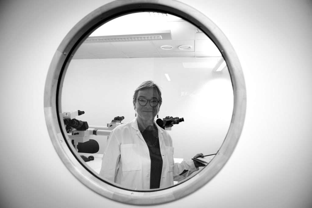 Kvinna i vit labbrock bakom ett runt fönster
