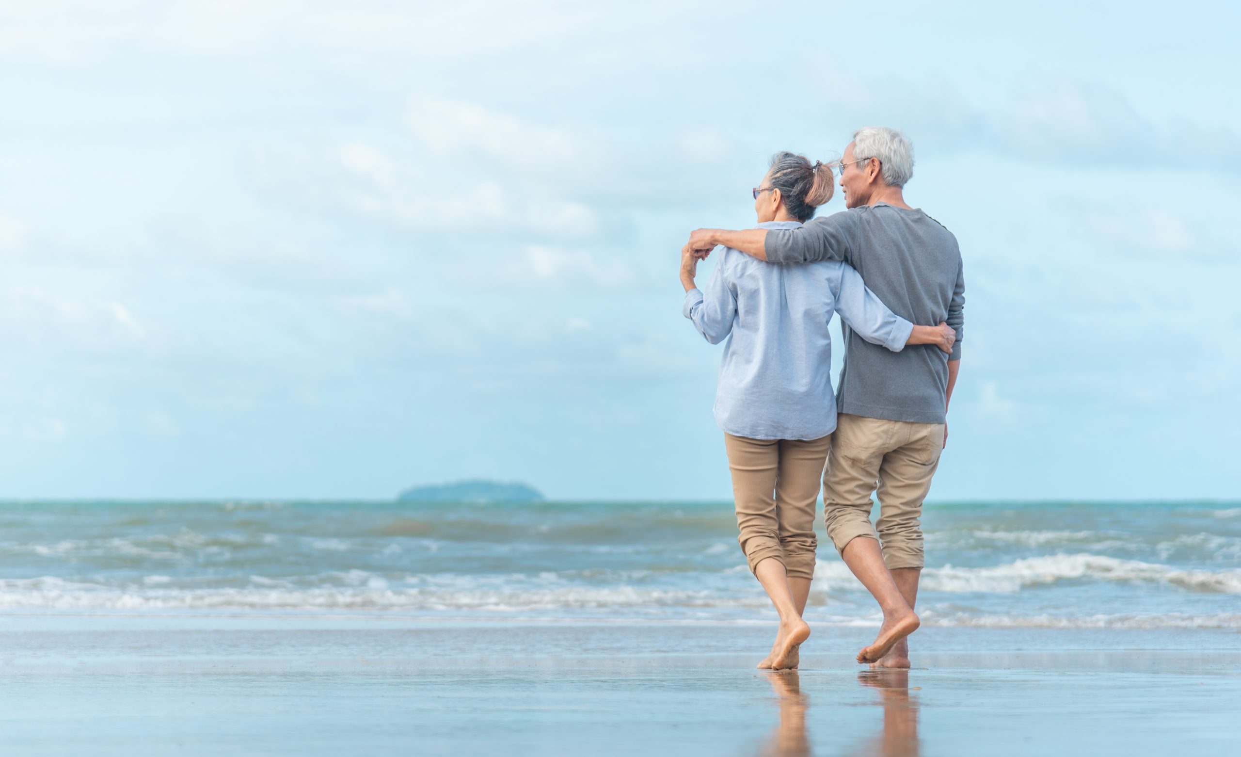 Äldre par går tillsammans på strand.