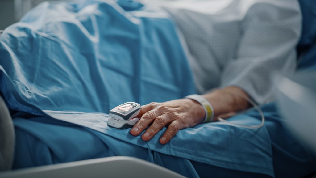äldre person i sjukhussäng med en syremätare på fingret