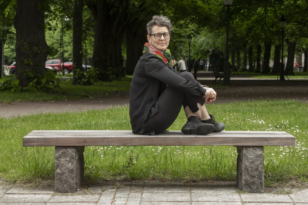 Tove Lundberg sitter på en bänk i en parl med benen uppdragna framför sig
