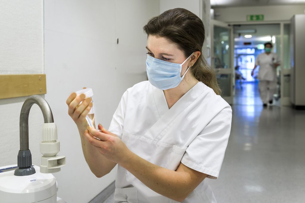 Kvinna med munskydd och vita sjukhuskläder med apparat.