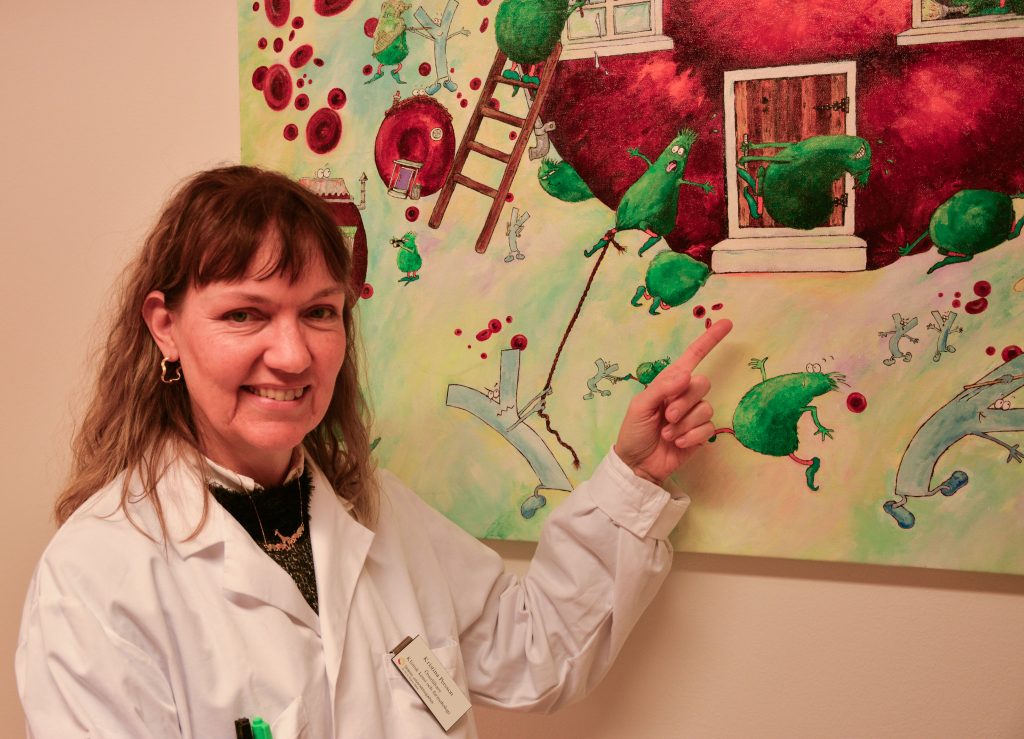 Kvinna i vit labbrock står framför en tavla med skämtsam avbildning av parasiter