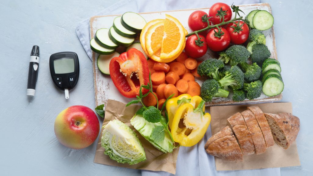 frukt och grönsaker upplagda på ett bord. Bredvid en glukosmätare