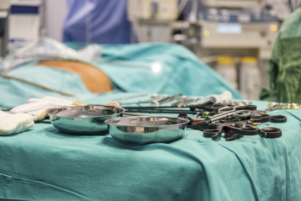 kirurgiska instrument upplagda på grön duk. Patient i bakgrunden blurrad