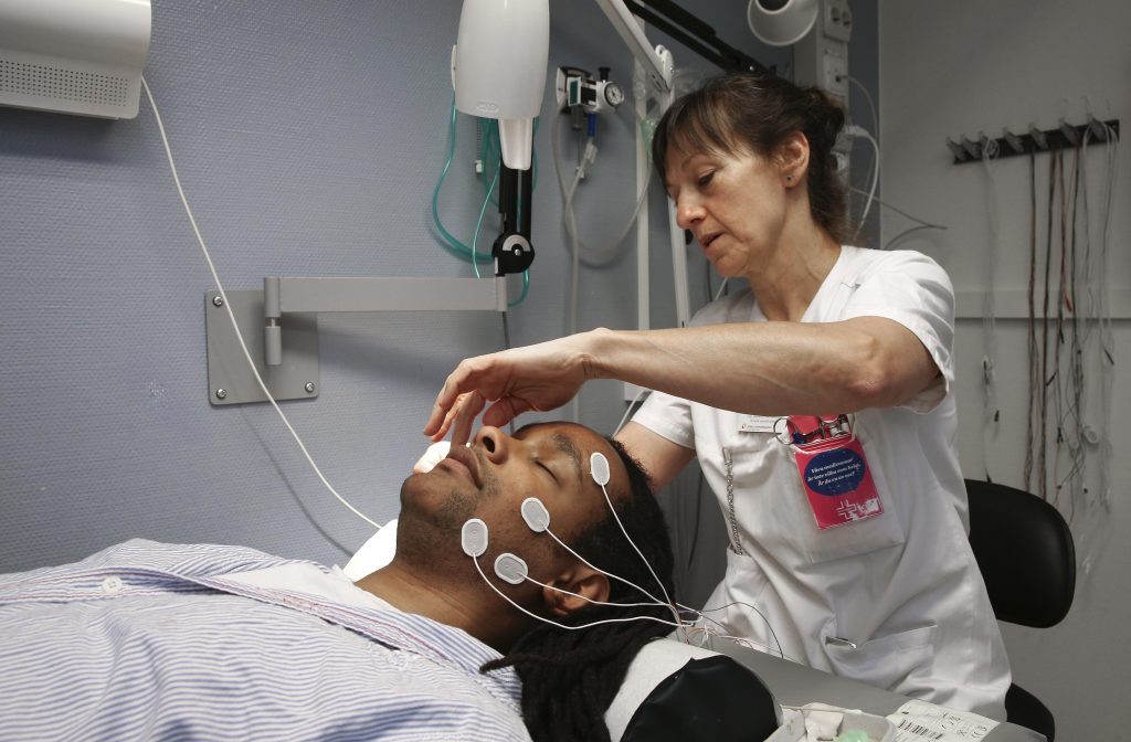 Kvinna i vita sjukvårdskläder sätter fast elektroder i ansiktet på patient som ligger på brits.