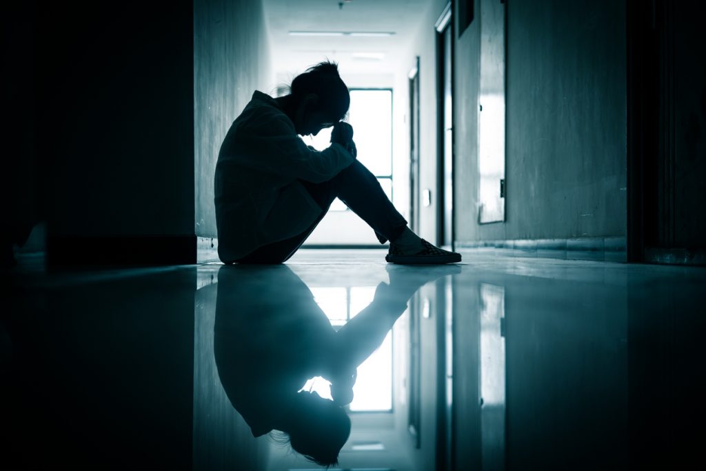 siluett av tonårsflicka som sitter på ettgolv i en korridor med huvudet lutat i armarna
