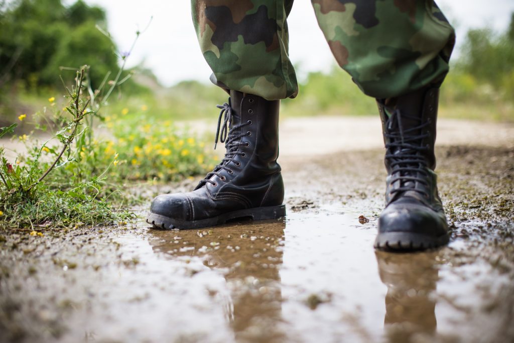 På bilden ses ett par ben i militärbyxor och kängor. Personen står i en vattenpöl