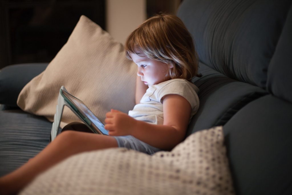 liten flicka sitter i Soffan och tittar på en digital skärm