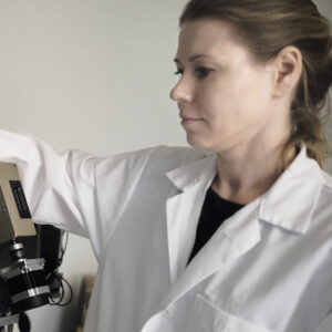 Kvinna i labbrock justerar lysande apparat.