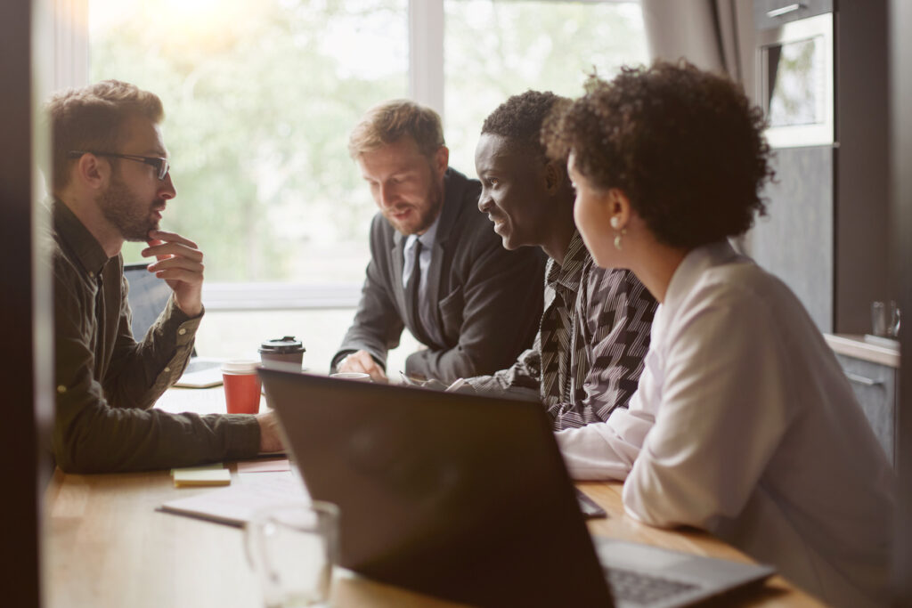 Arbetsplatsmöte. Fyra personer sitter runt ett mötesbord och pratar. 