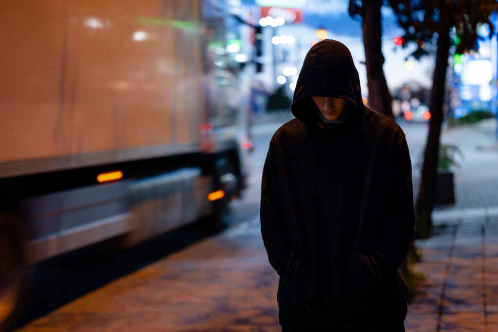 ung person i klädd hoodie med luvan uppdragen promenerar på gata. Ser hängig ut